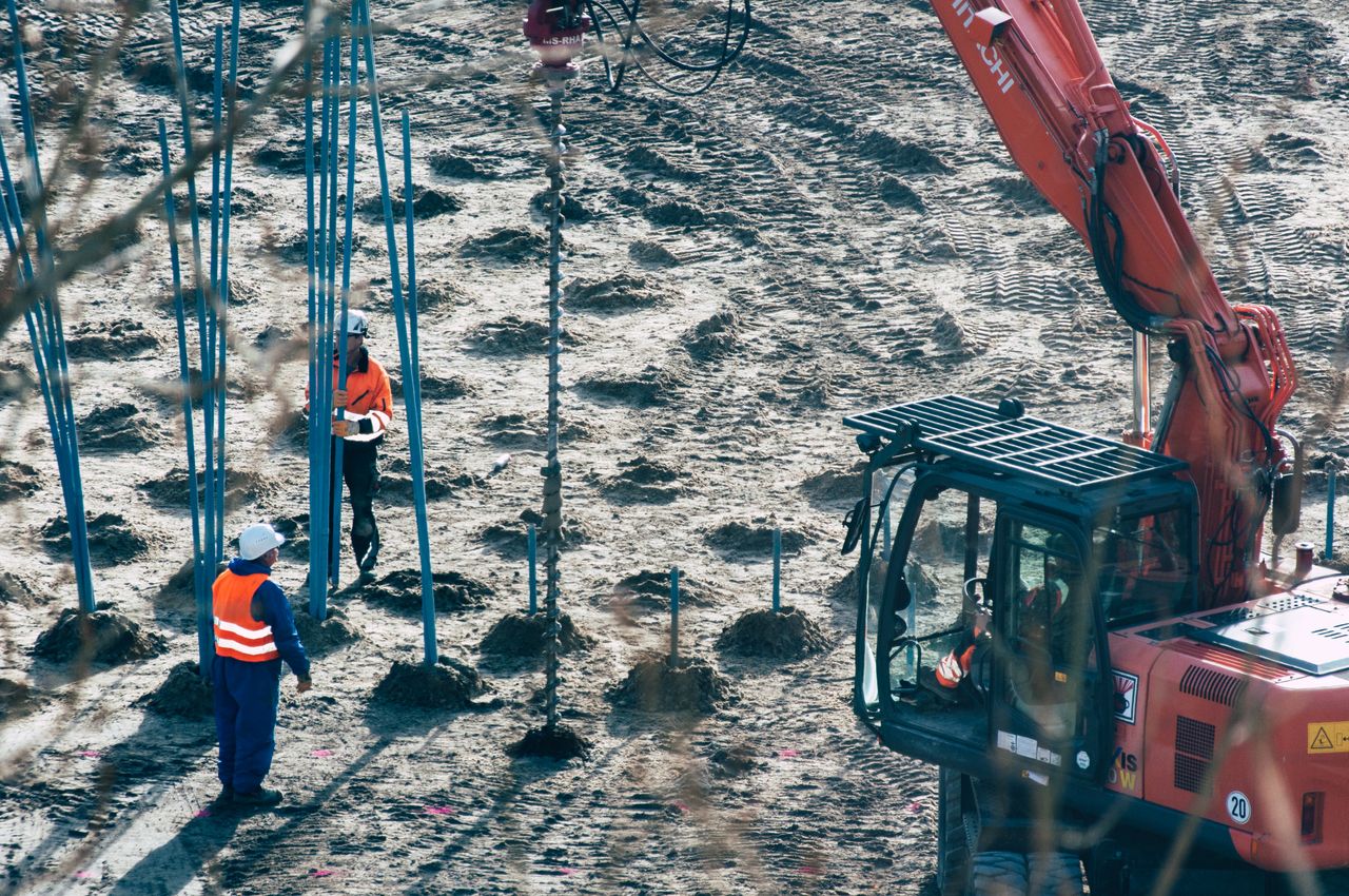 about-01 A construction site with workers and an excavator drilling holes in the ground.