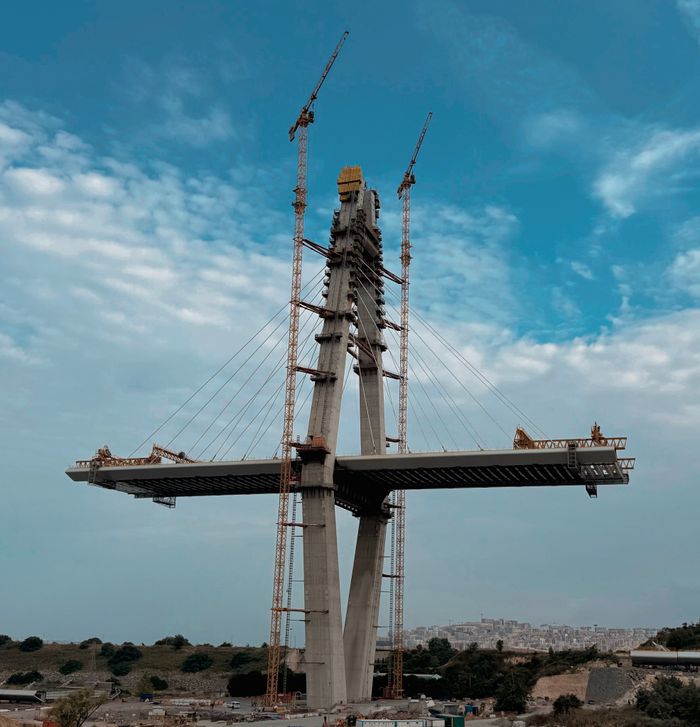 services-03 A modern suspension bridge under construction with cranes on a bright day.